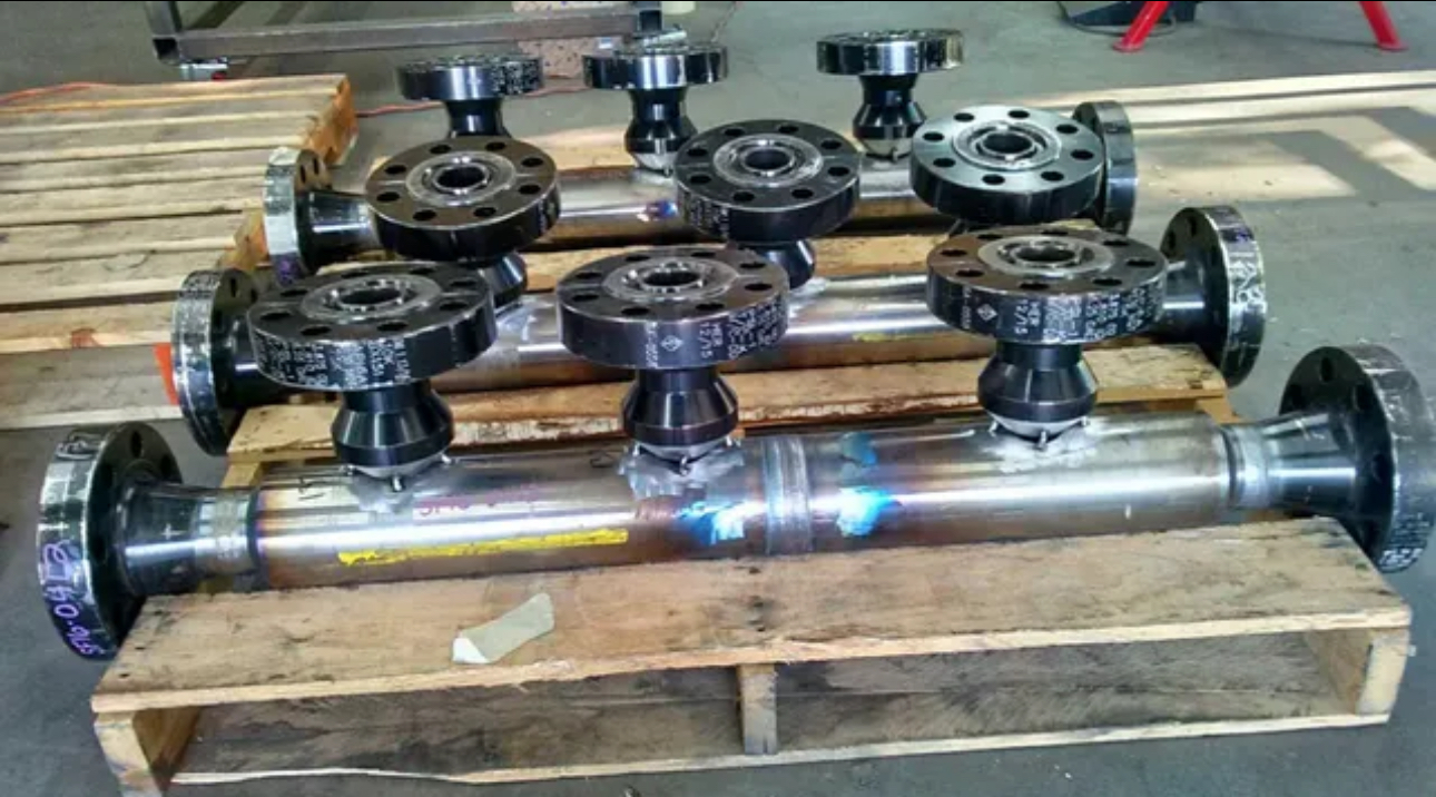 Batch of custom fabricated carbon steel pipe manifolds with flanged branch connections on a pallet.